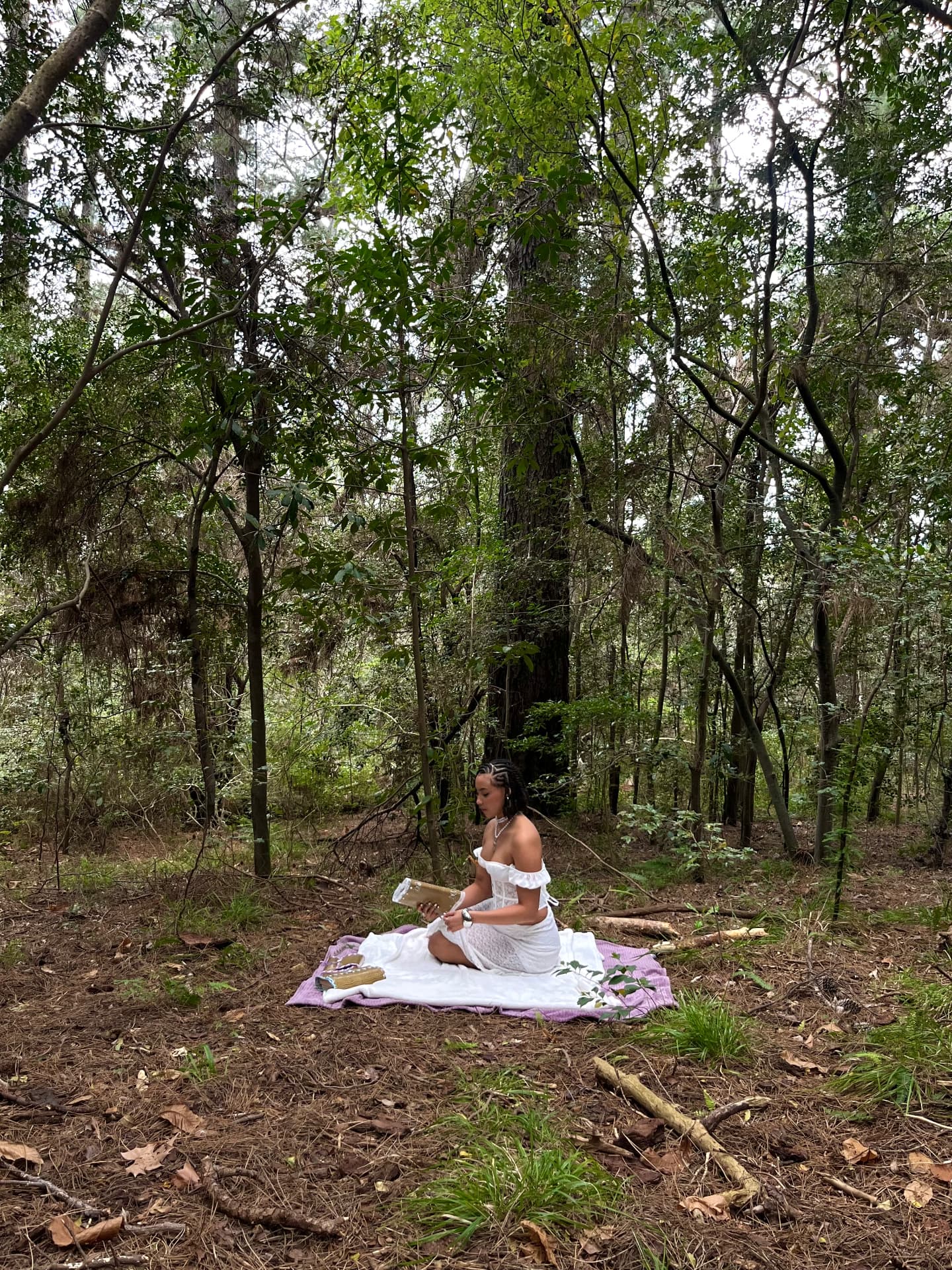 Woman sitting on a lavender blanket in the forest writing in a leather journal